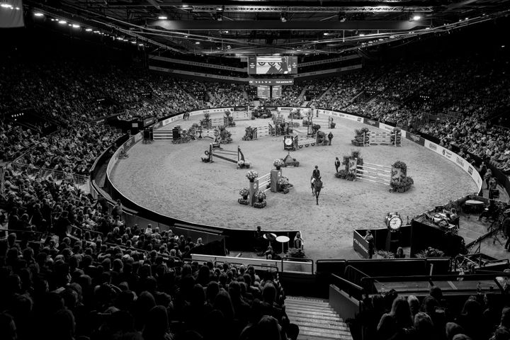 Svartvitt foto av en ryttartävling inomhus med publik runt en oval bana.