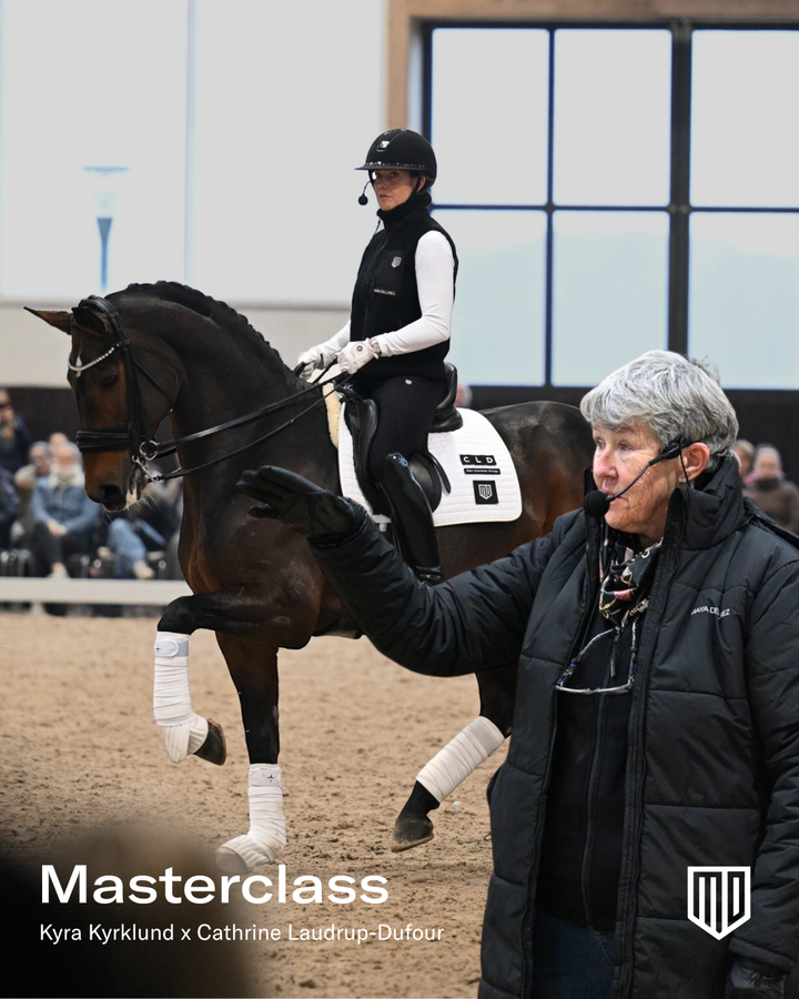 En person rider på en häst i en inomhusarena medan en instruktör ger vägledning. Många åskådare sitter i bakgrunden. Text på bilden: "Masterclass Kyra Kyrklund x Cathrine Laudrup-Dufour".
