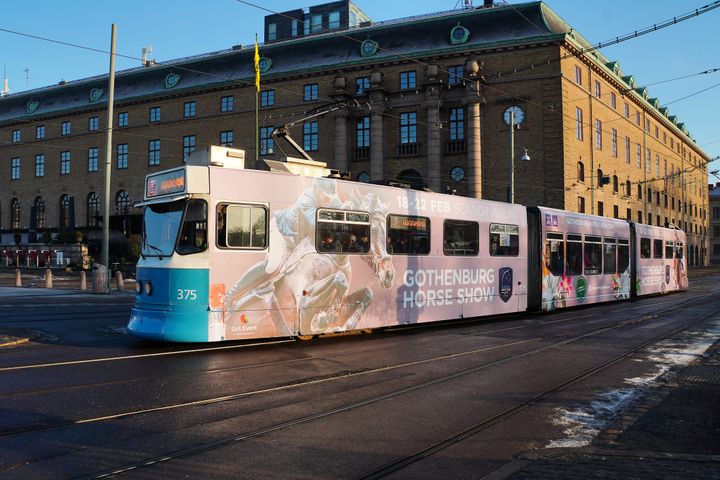 En spårvagn med reklam för Gothenburg Horse Show framför en klassisk byggnad i stadsmiljö.