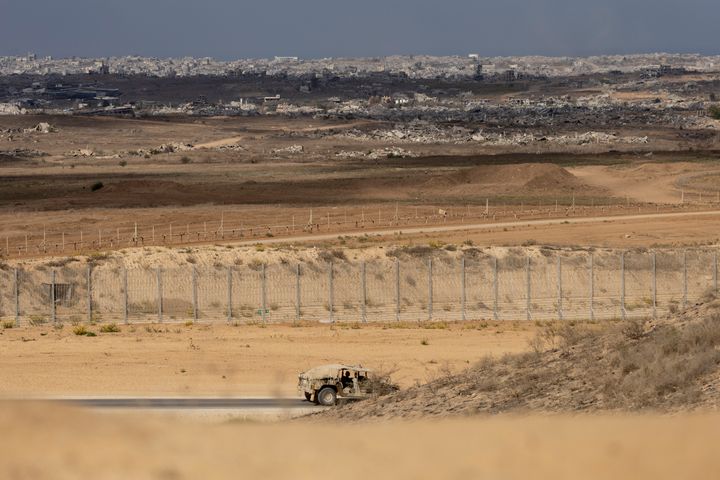 Utsikt mot Gaza från israeliskt territorium, med omfattande förstörelse synlig i stadsbebyggelsen på avstånd. Ett israeliskt militärfordon patrullerar området intill gränsstängslet.