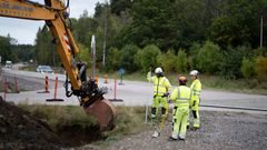 Arbetare i skyddskläder med en grävmaskin vid vägkant.