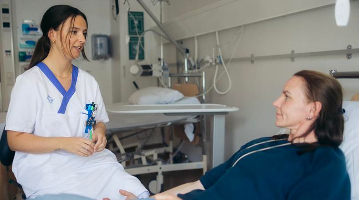 Vårdpersonal som pratar med en patient som ligger i en säng.