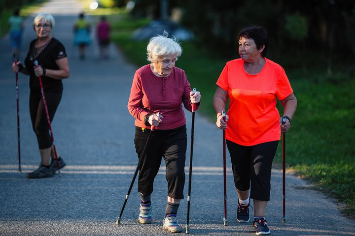 Tre personer promenerar med gångstavar på en asfalterad väg.