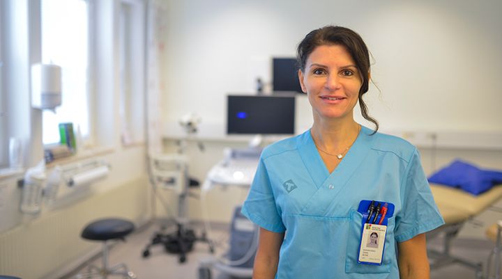 Leende vårdpersonal i blå arbetskläder i ett undersökningsrum.