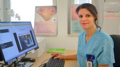 Vårdpersonal i blå arbetskläder arbetar vid en dator på en klinik.