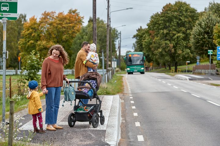 En familj med barn väntar på en buss vid en busshållplats.