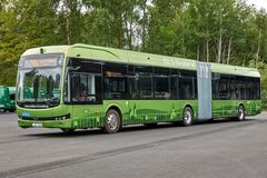 Grön ledad elbuss på en asfalterad yta, omgiven av träd.