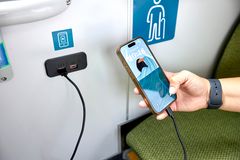 En person laddar mobiltelefonen via en USB-port på en buss.