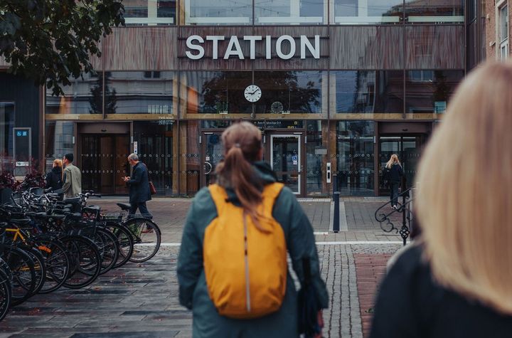 Två personer går mot en stationsbyggnad, med cyklar parkerade till vänster.
