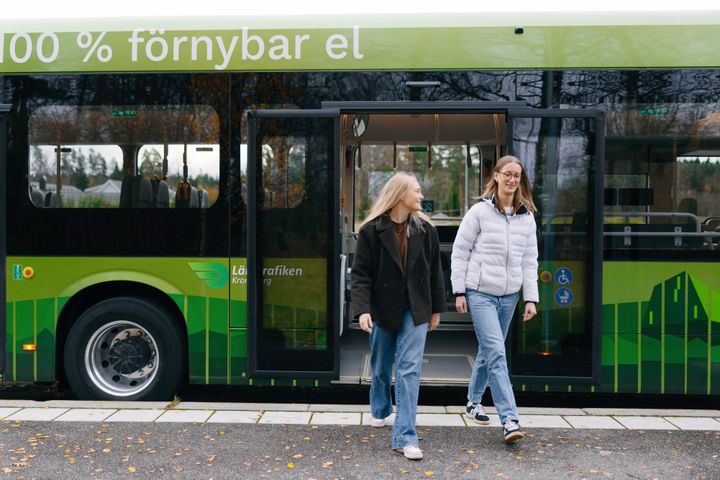 Två unga kvinnor går av en grön buss