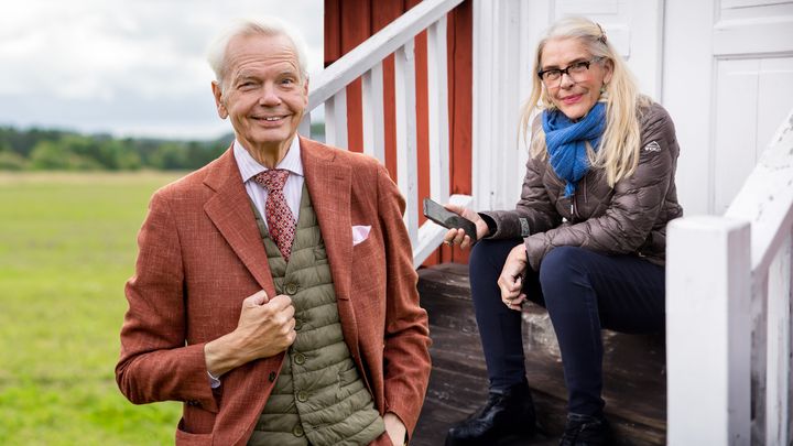 En man i kavaj står bredvid en kvinna som sitter på trappan utomhus.