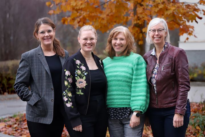 Gruppfoto på fyra leende kvinnor framför ett träd.