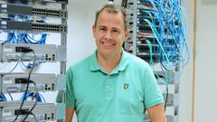 Man i turkos tröja framför ett teknikskåp med sladdar.