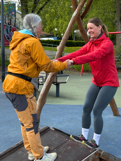 Två kvinnor balanserar och håller varandras händer på en lekplats.