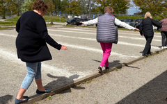 Kvinnor balanserar på smal bräda över grustäckt mark.