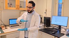 Man i vit rock står i laboratorium framför datorskärmar.