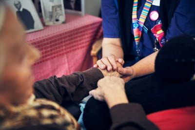 En sjuksköterska i kommunal hälso- och sjukvård håller en boende i handen.