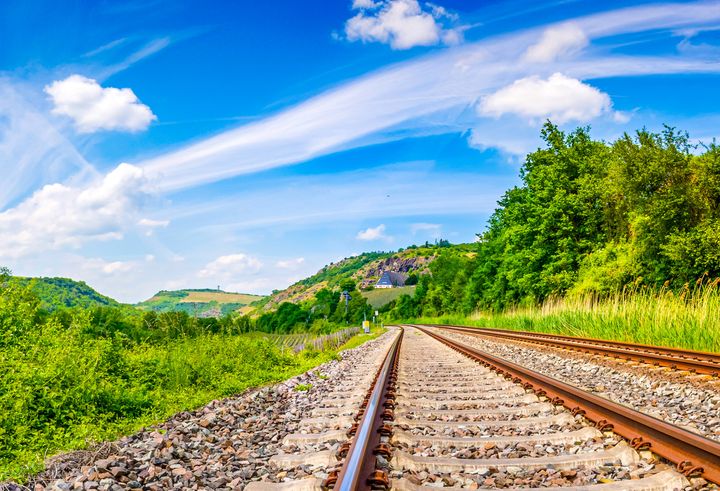 Järnväg med grönska bredvid järnvägen och blå himmel med vita moln.