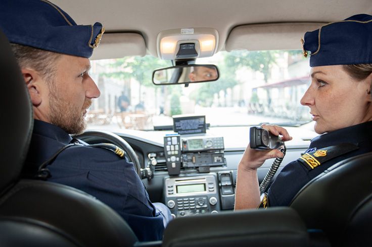 Två poliser i en polisbil som pratar lyssnar i polisbilens telefon.