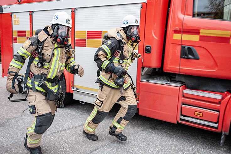 Två brandmän som springer vid sin brandbil i full utrustning.