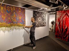 En person justerar stora, färgglada gobelänger som hänger på en vägg i ett galleri.