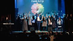 En grupp personer på scen med en färgglad blomma i bakgrunden och texten Funk Is Up