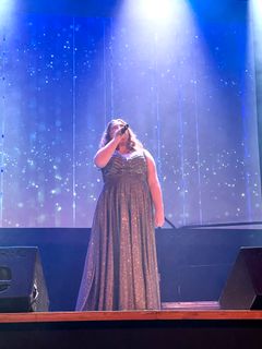 En kvinna på scen i lång glitterklänning. Blått ljus från strålkastare.