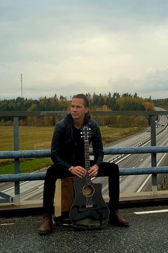 Man sitter med gitarr på ett räcke ovanför en motorväg.