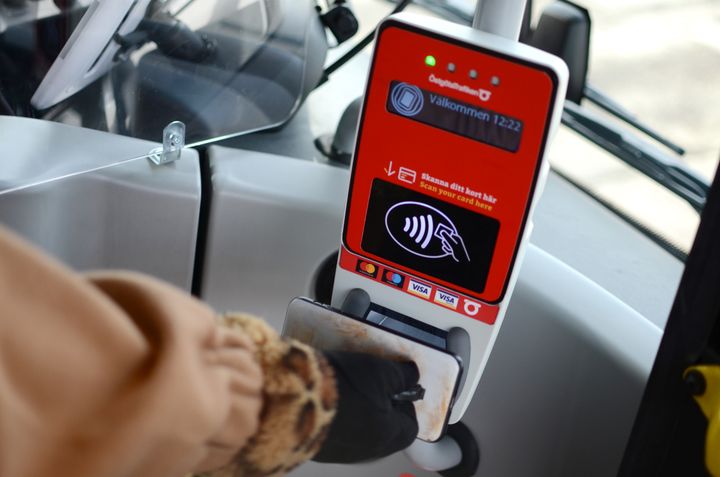 En arm som håller i en mobil mot en biljettläsare.