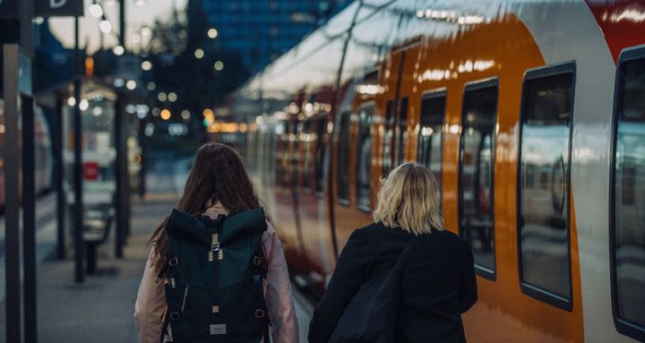 Ryggen av två tjejer som går på en perrong intil ett tåg.