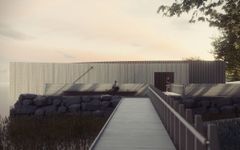 Modern byggnad med träfasad vid vatten, omgiven av stenar och växtlighet. Två personer syns vid byggnaden, en sittande och en stående.