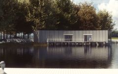 En modern byggnad med plåtfasad vid en sjö, omgiven av träd.