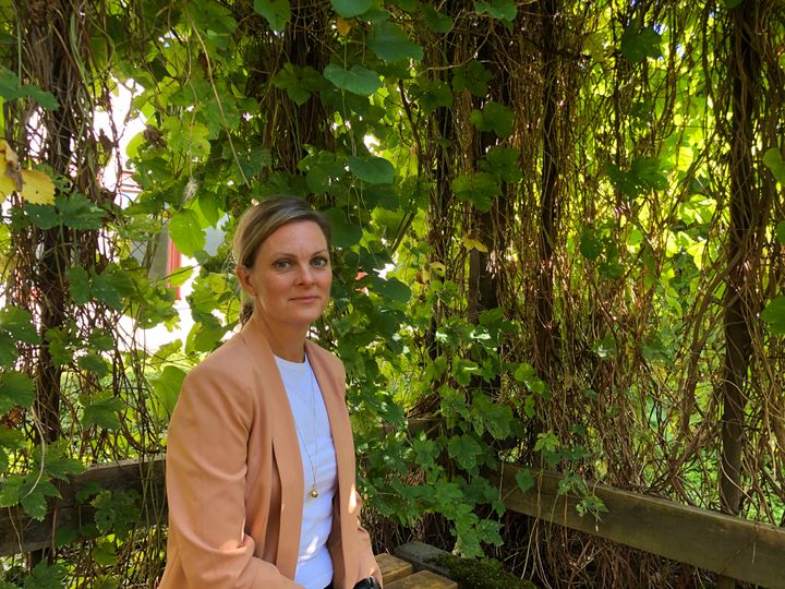 Anna-Karin Larsson sitter i en pergola med gröna blomrankor.