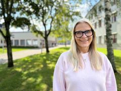 Kvinna i rosa tröja och glasögon framför gräsmatta med träd