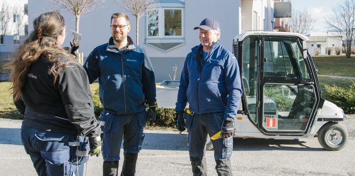 Tre personer diskuterar utomhus vid en mindre lastbil.