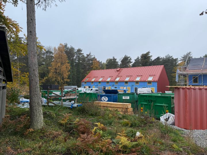 Byggarbetsplats med färgglada hus och containrar, omgiven av träd.
