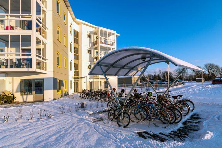 Bild av ett bostadsområde en vinterdag, cyklar står parkerade under ett tak i snön.