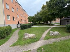 Bild av ett grönområde i kvarteret Vitkålen i Visby med gångvägar, buskar och två stenskulpturer på gräsmattan.
