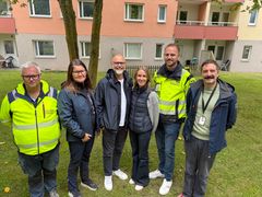 Gruppfoto av sex personer som står utomhus framför ett flerfamiljshus.