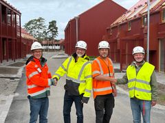 Fyra män i arbetskläder och hjälmar står framför en byggarbetsplats och skakar hand.