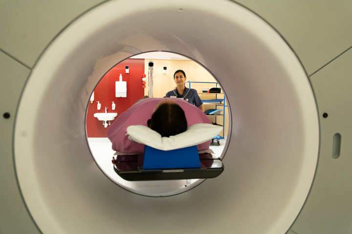 Strålbehandling på Karolinska Universitetssjukhuset. En patient ligger i på brits i maskinen, där strålbehandlingen med röntgenbildtagning görs. En strålbehandlingssjuksköterska syns bakom patienten.