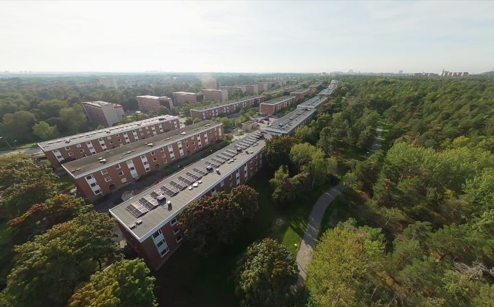 Flygfoto av lägenhetsbyggnader i Bagarmossen med solceller på taken, omgivna av grönska.