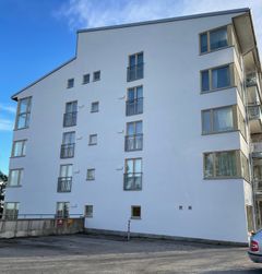 En vit, nytvättad flervåningsbyggnad med stora fönster och klarblå himmel i bakgrunden.