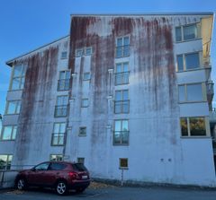 En vit byggnad med synliga mörka fläckar av rödalger på fasaden, före rengöring.