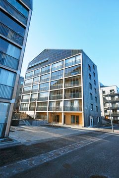 En modern flerfamiljsbyggnad med stora fönster och solpaneler på taket, belägen i ett urbant område.