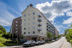 Flerfamiljshus längs en gata i Stockholm, med parkerade bilar framför.