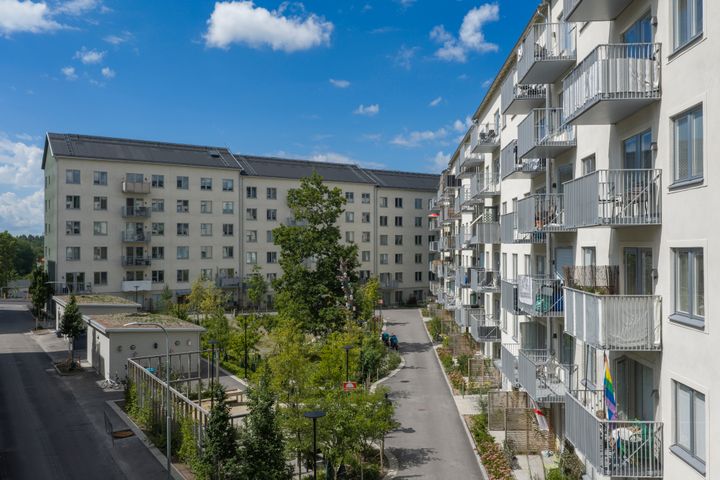 Flervåningshus med grönskande gård, växtbäddar och gångväg.