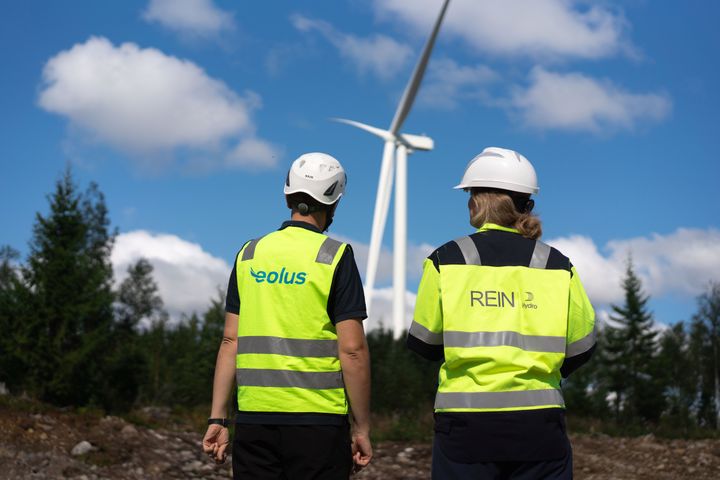 Två personer i varselväst framför ett vindkraftverk