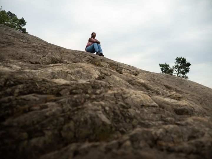En person sitter ensam på en stenig klippa under en mulen himmel.