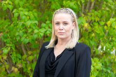 Kvinna i svart kavaj står framför gröna buskar.